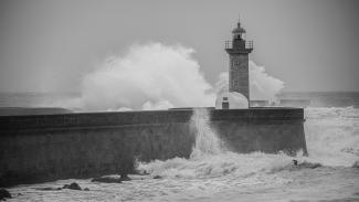 a black and white photo of waves crashing against a lighthouse by Gary Walker-Jones courtesy of Unsplash.